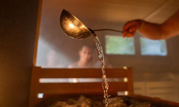 Hand pouring water over rocks in steam room 