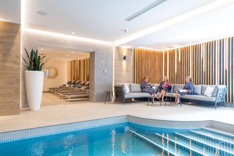 Three ladies sat on sofa near indoor pool 