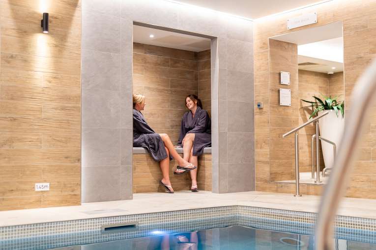 2 women sat on the edge of the pool talking at Source Spa