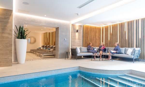 Three ladies sat on sofa near indoor pool 