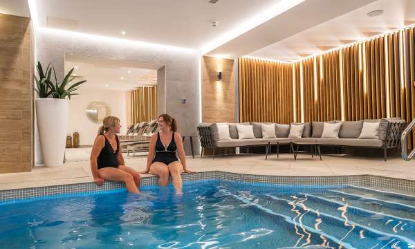 2 women sat on the edge of the pool talking at Source Spa