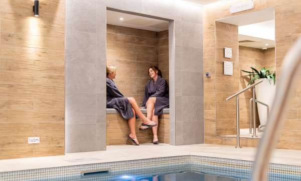 2 women sat on the edge of the pool talking at Source Spa