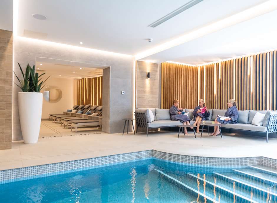 Three ladies sat on sofa near indoor pool 