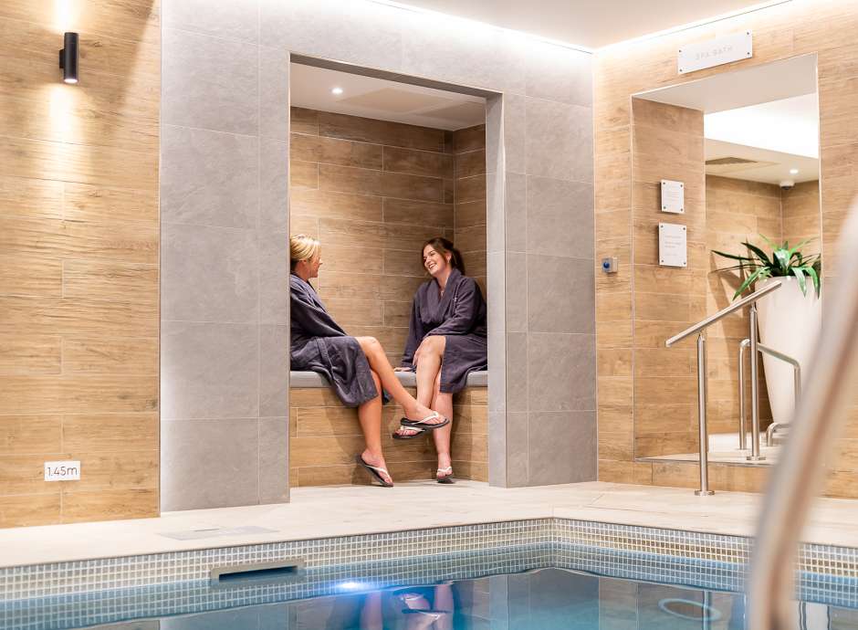 2 women sat on the edge of the pool talking at Source Spa